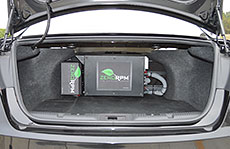A photo of an open vehicle trunk with a black auxiliary battery pack inside.